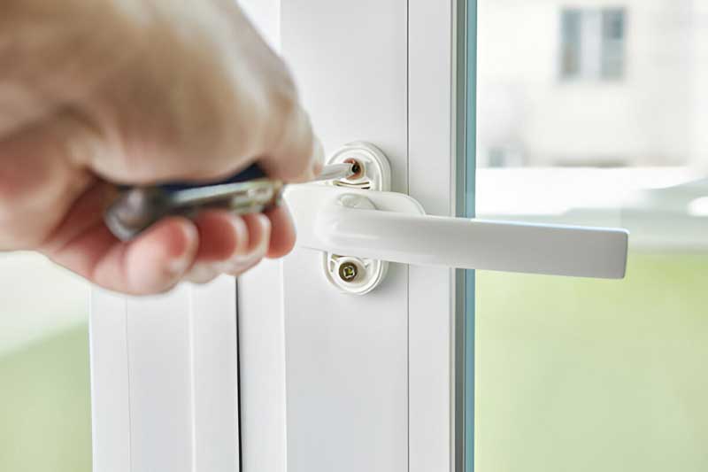 Hand using screwdriver to install or repair a white door lock, emphasizing residential security services by Tiger Locksmith.